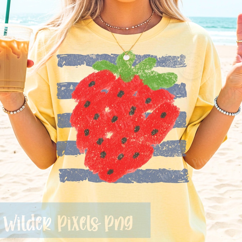 Op de afbeelding: Geel T-shirt met een grote rode aardbei-afbeelding en blauwe horizontale strepen. De aardbei heeft zwarte zaden en groene bladeren. De tekst "Wilder Pixels Png" staat onderaan.