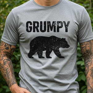 May include: A gray t-shirt with the word "GRUMPY" in large, distressed black letters above a black bear silhouette. The bear is walking to the right. The shirt is short-sleeved.