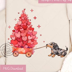 May include: A cream-colored sweatshirt featuring a watercolor illustration of a dachshund pulling a red wagon filled with heart-shaped decorations. Pink stars and the text "PNG Download" are also visible.