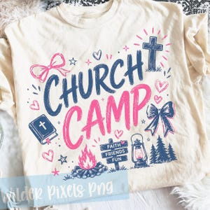 May include: Cream-coloured t-shirt with a graphic design featuring the words "CHURCH CAMP" in blue and pink. The design includes a cross, hearts, bows, a campfire, a lantern, and the text "Faith Friends Fun".