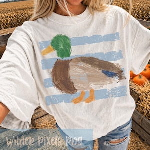 Pu&ograve; includere: T-shirt bianco sporco con un disegno di anatra dipinta, con testa verde, corpo marrone e becco e zampe gialle. L'anatra &egrave; posta su strisce orizzontali azzurre. Il testo "Wilder Pixels Png" &egrave; in basso.