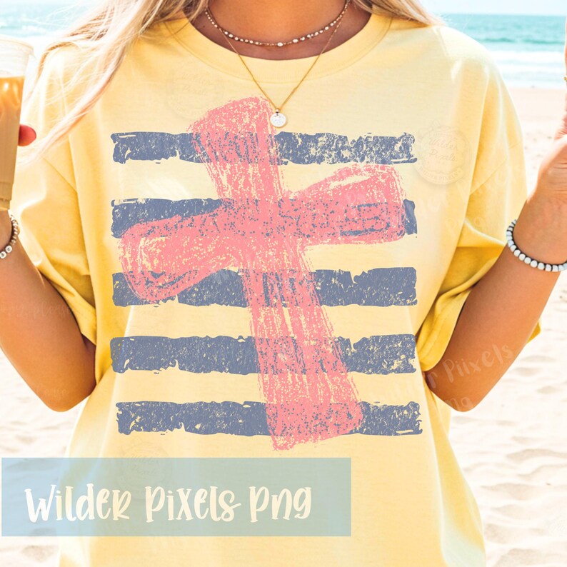 May include: Yellow t-shirt with a distressed pink cross design over blue stripes. The shirt has a relaxed fit and is worn on a beach. The text "Wilder Pixels Png" is at the bottom of the image.