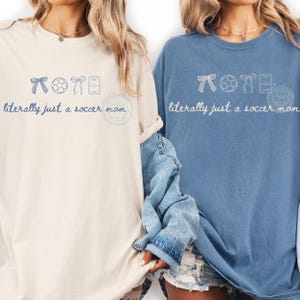 May include: Two long-sleeved t-shirts, one cream and one blue, with the text "literally just a soccer mom." Each shirt has a soccer-themed graphic above the text. The cream shirt is on the left, and the blue shirt is on the right.