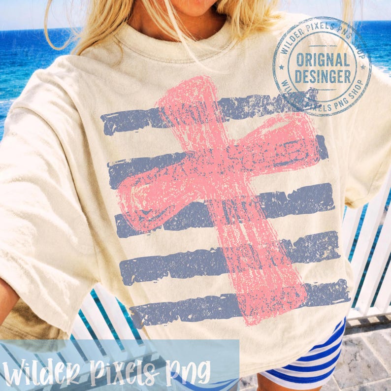 May include: Cream-colored t-shirt featuring a distressed pink cross design over blue horizontal stripes. The shirt has a vintage, worn look. The text "Wilder Pixels Png" is at the bottom of the shirt. The shirt also has a circular stamp that says "Original Desinger".