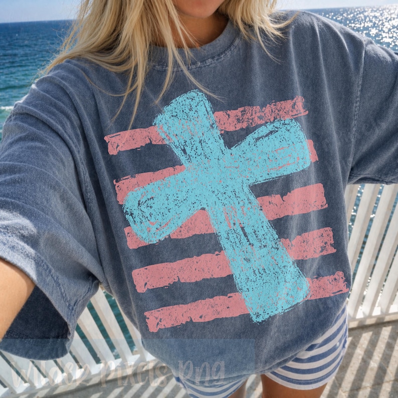 May include: A blue t-shirt with a large, light blue cross design over pink horizontal stripes. The shirt has a slightly faded, vintage look. The overall theme is religious or spiritual.