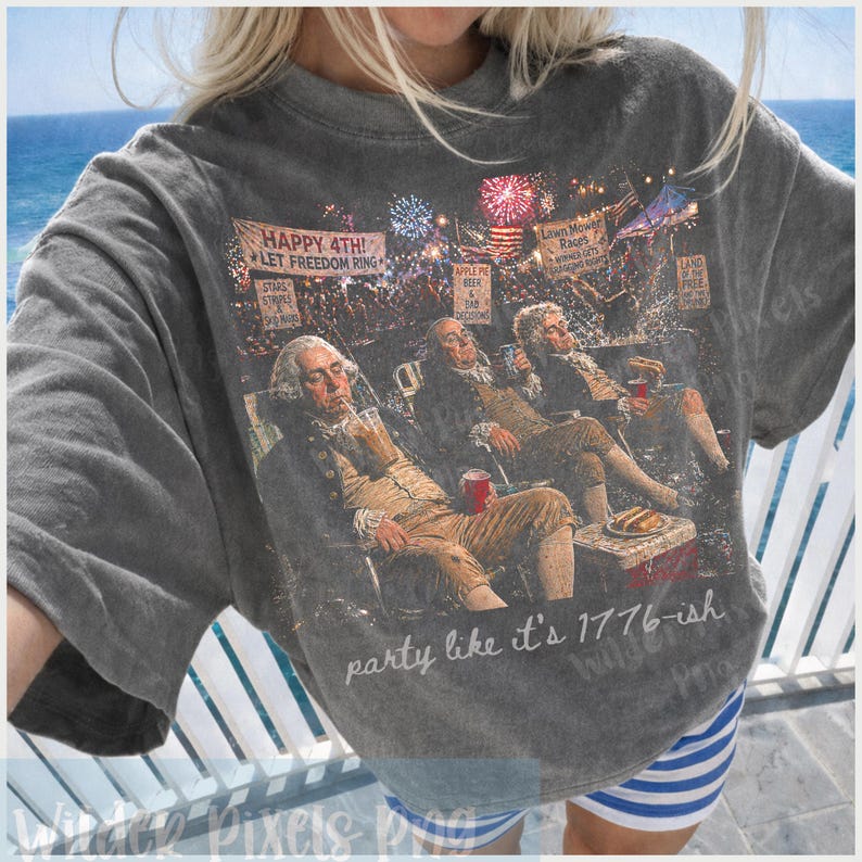 Puede incluir: Una camiseta gris con un gr&aacute;fico de figuras hist&oacute;ricas relaj&aacute;ndose con bebidas y comida, con fuegos artificiales de fondo. El texto "HAPPY 4TH! LET FREEDOM RING" y "party like it's 1776-ish" tambi&eacute;n es visible.