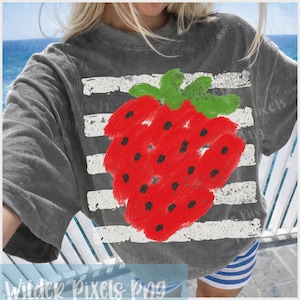 Op de afbeelding: Grijs T-shirt met een groot, handgetekend rood aardbei-ontwerp, met zwarte zaden en groene bladeren. De aardbei is geplaatst tegen witte horizontale strepen. De tekst "Wilder Pixels png" staat onderaan de afbeelding.