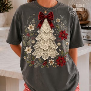 Pu&ograve; includere: Una t-shirt grigio antracite con la grafica di un albero di Natale realizzato in pizzo color crema, sormontato da un grande fiocco rosso scuro. Il disegno &egrave; circondato da stelle di Natale rosse, fiori bianchi, foglie di agrifoglio e decorazioni oro.