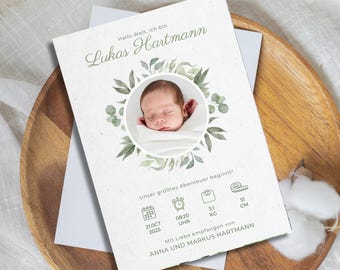 May include: A birth announcement card with a photo of a baby surrounded by a green floral wreath. The card includes the baby's name, Lukas Hartmann, and details such as date, time, weight (3.1 kg), and length (51 cm).