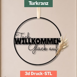 Könnte beinhalten: Ein schwarzer, kreisförmiger Wandbehang mit dem Schriftzug "Tach", "WILLKOMMEN" und "Glück auf" in einer Kombination aus Schreib- und Blockschrift. Ein kleines Bündel getrockneter beiger Gräser ist an der rechten Seite des Rings befestigt.