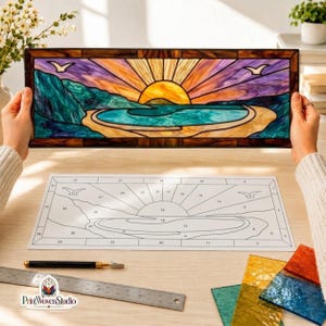 Puede incluir: Un panel rectangular de vidriera que representa una puesta de sol sobre una playa con un océano turquesa, acantilados verdes y dos aves. Debajo del panel hay una plantilla de papel numerada, un cortador de vidrio, una regla y láminas de vidrio.