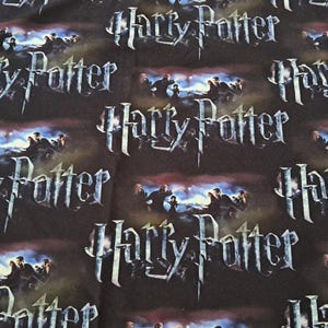 Op de afbeelding: Donkere stof met de woorden "Harry Potter" in zilverkleur herhaald. De achtergrond toont een scène met figuren en een blauw-witte gloed, wat een fantasiethema creëert.