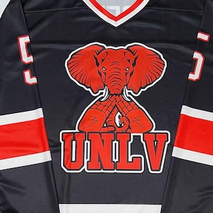 K&ouml;nnte beinhalten: Schwarzes Langarm-Trikot mit roten und wei&szlig;en Akzenten. Es zeigt eine rote Elefanten-Grafik und die wei&szlig;en Buchstaben "UNLV". Das Trikot hat einen V-Ausschnitt mit rotem und wei&szlig;em Besatz und die Nummer "5" auf den &Auml;rmeln.