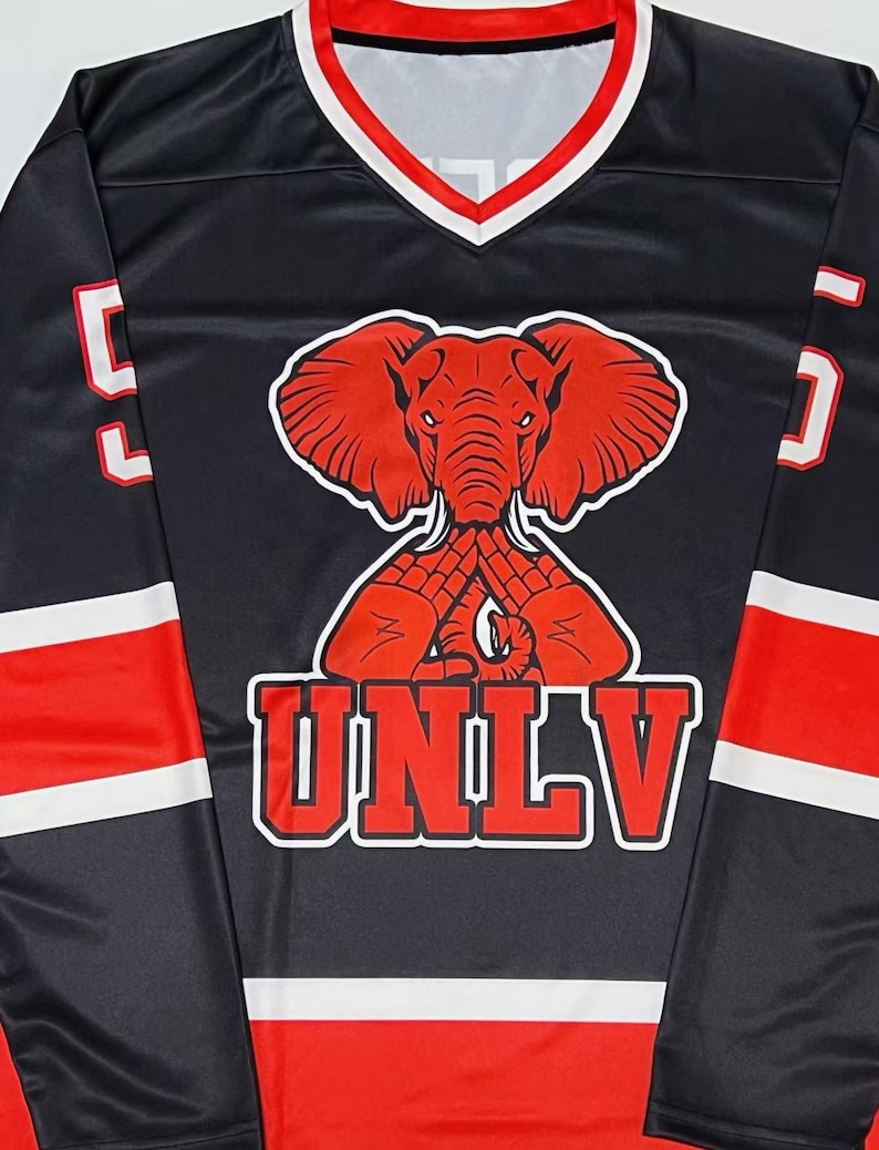 K&ouml;nnte beinhalten: Schwarzes Langarm-Trikot mit roten und wei&szlig;en Akzenten. Es zeigt eine rote Elefanten-Grafik und die wei&szlig;en Buchstaben "UNLV". Das Trikot hat einen V-Ausschnitt mit rotem und wei&szlig;em Besatz und die Nummer "5" auf den &Auml;rmeln.