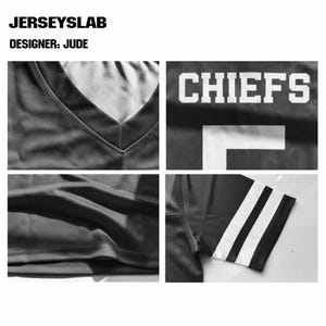 Pu&ograve; includere: Una maglia sportiva nera con scollo a V, scritte bianche in stampatello che recitano CHIEFS e un numero bianco sul davanti. Le maniche sono decorate con due strisce bianche orizzontali. Il testo JERSEYSLAB e DESIGNER: JUDE appare in alto.