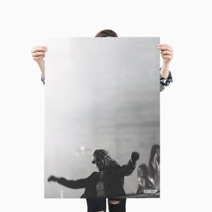 May include: Black and white poster featuring a person with long hair and sunglasses, arms outstretched in a dynamic pose. The image has a blurred background and a parental advisory label in the lower right corner.
