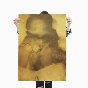May include: A sepia-toned print featuring a blurred image of a person with a fur collar and jewelry. The artwork is held by a person wearing a plaid shirt and black jeans. The print has a vintage aesthetic.