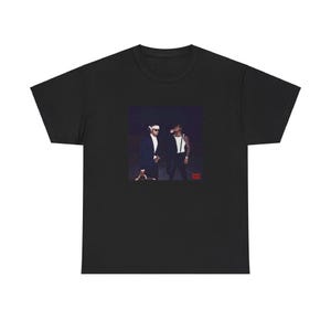 May include: Black t-shirt featuring a graphic of two people in suits and sunglasses. The image is a dark, moody photograph. The t-shirt is made of a soft, comfortable material.