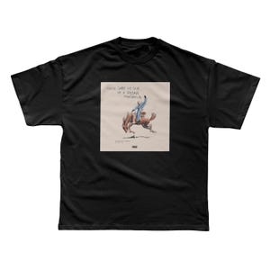 May include: Black t-shirt featuring a square graphic with a rider on a bucking bronco. The graphic includes the text "NADIE SABE LO QUE VA A PASAR MAÑANA" in white. The design is in shades of brown, blue, and white.