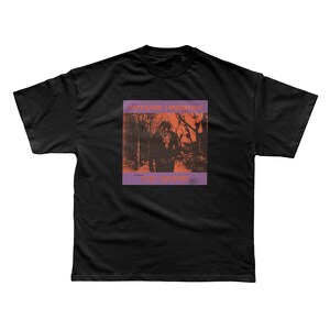 Może przedstawiać: Czarny t-shirt z prostokątną grafiką. Grafika zawiera tekst "FUTURE HNDRXX" nad "THE WIZARD". Grafika jest pomarańczowo-fioletowa i przedstawia osobę w lesie.