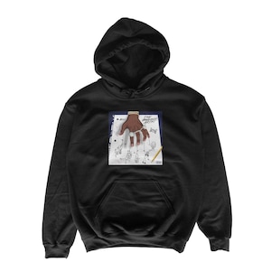 May include: Black hoodie with a front graphic. The graphic features a hand with a gold ring, holding strings attached to stick figures, with the text "THE PUPPET ARTIST". The hoodie has a hood and a front pocket.