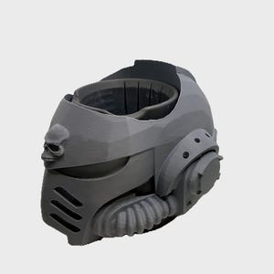 May include: A gray, futuristic helmet with a skull emblem on the side. The helmet has a complex design with vents, a circular component, and a ribbed section. The overall aesthetic suggests a science fiction or cosplay theme.