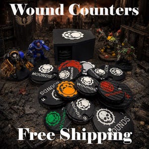 May include: A collection of circular black, red, orange, and green wound counter tokens featuring skull icons and the text WOUNDS, accompanied by a black storage box. The tokens are displayed alongside two miniature painted warrior figures.
