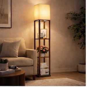 May include: A tall, wooden floor lamp with a square, off-white lampshade. The lamp has built-in shelves holding books, a framed picture, and a potted plant. The lamp is in a living room setting with a beige sofa and a round coffee table.