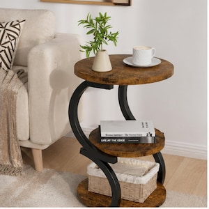 May include: A three-tiered side table with a dark brown, distressed finish. The table has a black metal frame with curved supports. The top tier holds a cup and saucer, a vase with greenery. The middle tier has books, and the bottom tier has a basket.