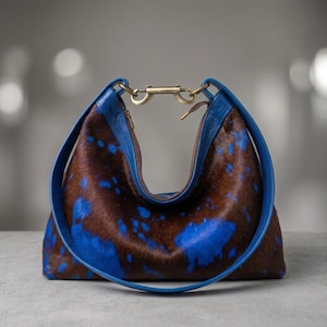 Cowhide hobo bag in brown and blue cow print with blue leather trim and brass toggle clasp, oversized slouchy shoulder bag for everyday western boho style.