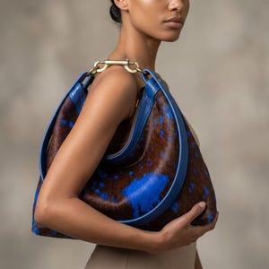 Cowhide hobo bag in brown and blue cow print with blue leather trim and brass toggle clasp, oversized slouchy shoulder bag for everyday western boho style.
