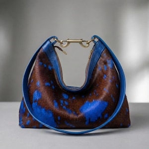 Cowhide hobo bag in brown and blue cow print with blue leather trim and brass toggle clasp, oversized slouchy shoulder bag for everyday western boho style.