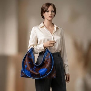 Cowhide hobo bag in brown and blue cow print with blue leather trim and brass toggle clasp, oversized slouchy shoulder bag for everyday western boho style.