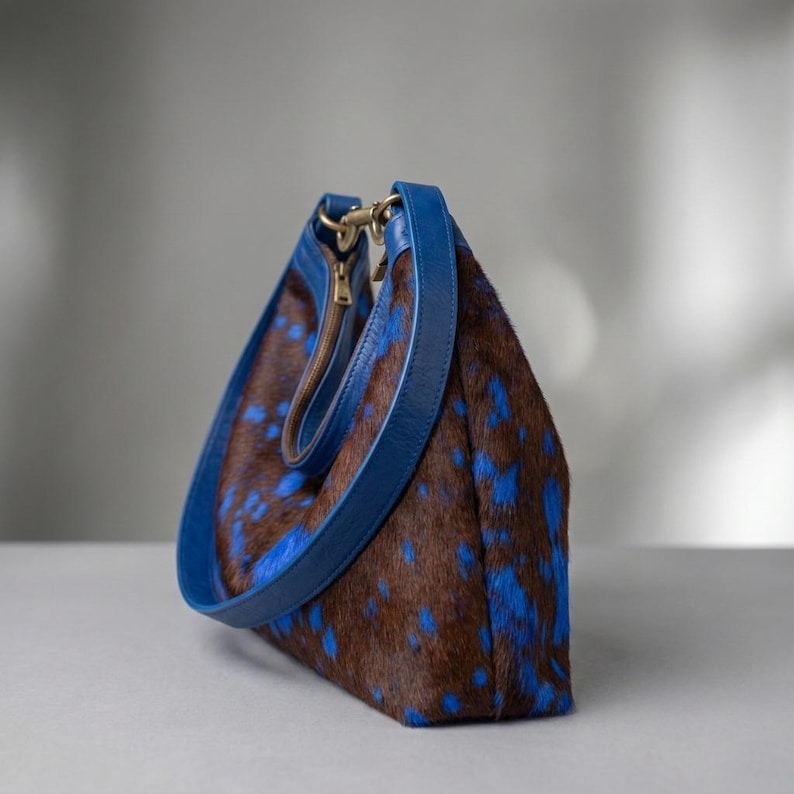 Cowhide hobo bag in brown and blue cow print with blue leather trim and brass toggle clasp, oversized slouchy shoulder bag for everyday western boho style.