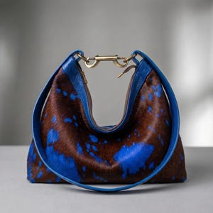 Cowhide hobo bag in brown and blue cow print with blue leather trim and brass toggle clasp, oversized slouchy shoulder bag for everyday western boho style.