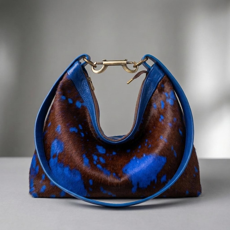 Cowhide hobo bag in brown and blue cow print with blue leather trim and brass toggle clasp, oversized slouchy shoulder bag for everyday western boho style.