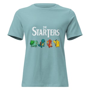 Puede incluir: Camiseta azul claro con la inscripción "The Starters" y un gráfico de cuatro personajes de dibujos animados: Bulbasaur, Squirtle, Charmander y Pikachu. La camiseta es de material suave.