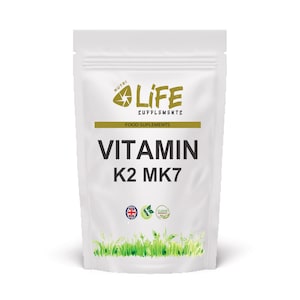 Op de afbeelding: Witte zak van Nutri Life Supplements Vitamine K2 MK7. De verpakking bevat het merklogo, de productnaam en de woorden "Food Supplements". De onderkant van de zak heeft een groen grasontwerp en drie kleine pictogrammen.