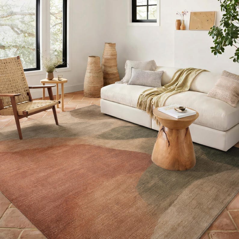 a cozy living room with a large white sofa, a woven chair, and a wooden side table. The room is decorated with various natural elements, such as a woven basket, a potted plant, and a vase. The floor is covered with a rug featuring a warm, earthy color palette.