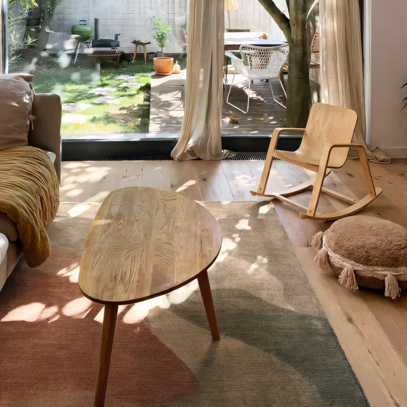 a cozy living room with a wooden rocking chair, a wooden coffee table, and a large window overlooking a backyard.