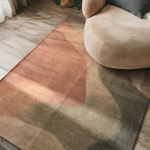 a rug with a geometric pattern in shades of orange, green, and beige, placed on a wooden floor next to a beige armchair.