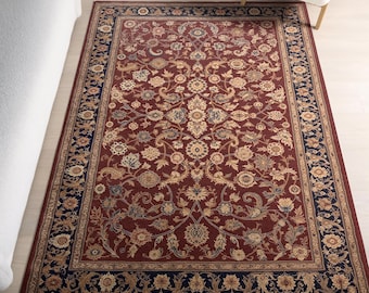 May include: A rectangular area rug featuring a deep red centre field with an intricate floral and vine pattern in shades of cream, tan, and blue. The rug is framed by a wide, dark navy blue border decorated with repeating floral motifs.