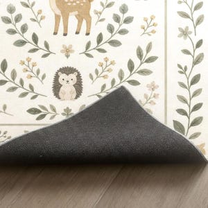 a rug with a forest-themed design, including a deer, hedgehog, and flowers. The rug is placed on a wooden floor, and there is a black rubber mat in front of it.