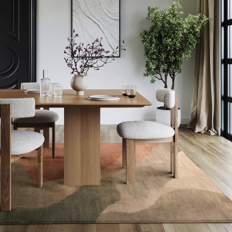 a modern dining room with a wooden table, white upholstered chairs, and a large window with a plant. The room has a minimalist and contemporary design, with a neutral color palette and clean lines.
