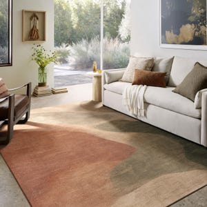 a cozy living room with a large window overlooking a garden, featuring a white sofa, a brown and orange rug, and a wooden side table with a vase of flowers.
