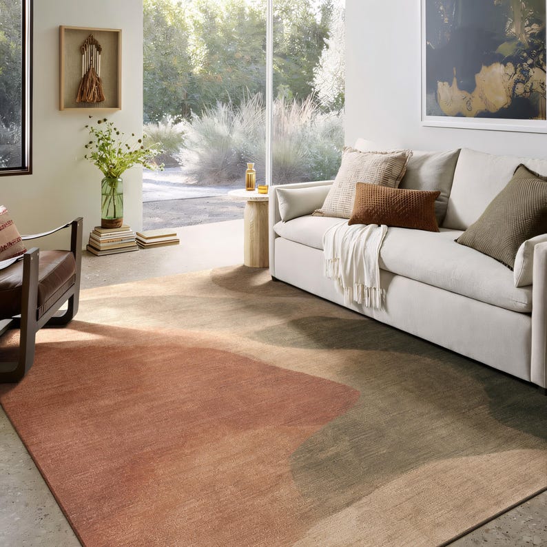 a cozy living room with a large window overlooking a garden, featuring a white sofa, a brown and orange rug, and a wooden side table with a vase of flowers.