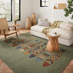 a cozy living room with a large, colorful rug featuring a fish design in various shades of green, blue, and orange. The room is furnished with a white sofa, a wooden chair, and a wooden side table. The room also includes a window, a plant, and decorative vases, creating a warm and inviting atmosphere.