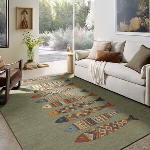 a cozy living room with a large window overlooking a garden. The room is furnished with a white sofa, a wooden coffee table, and a colorful fish-patterned rug. The room is decorated with various books, a vase of flowers, and a painting on the wall.