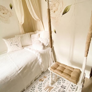 May include: A white bed with a canopy, decorative pillows, and a hanging swing seat with a tan cushion. The floor features a rectangular rug with illustrations of a deer, fox, raccoon, and hedgehog surrounded by green leaves and floral patterns.