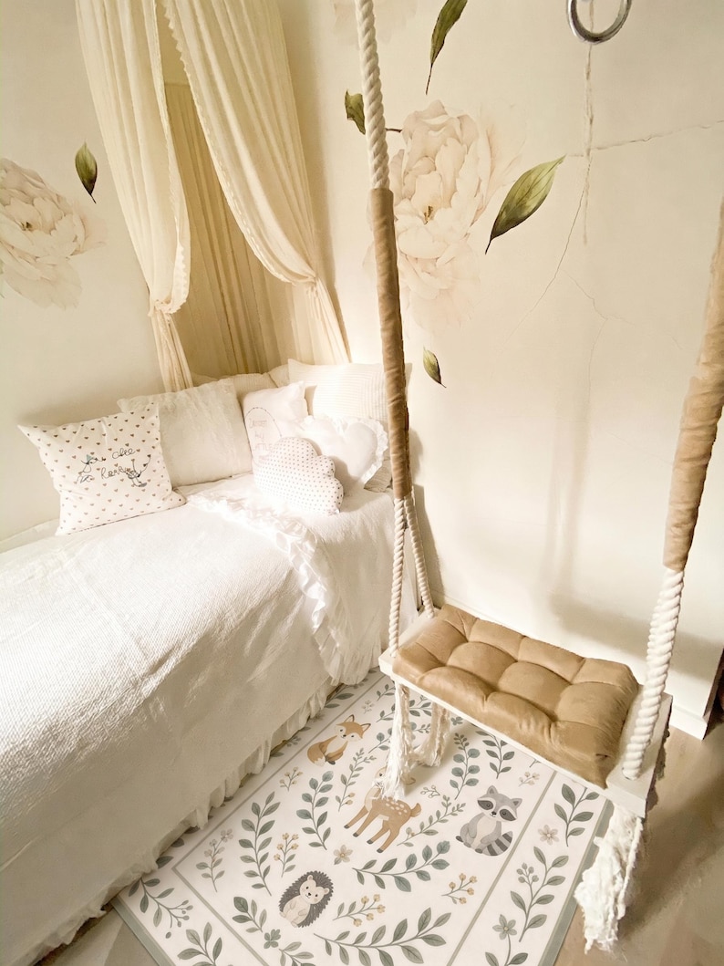 May include: A white bed with a canopy, decorative pillows, and a hanging swing seat with a tan cushion. The floor features a rectangular rug with illustrations of a deer, fox, raccoon, and hedgehog surrounded by green leaves and floral patterns.
